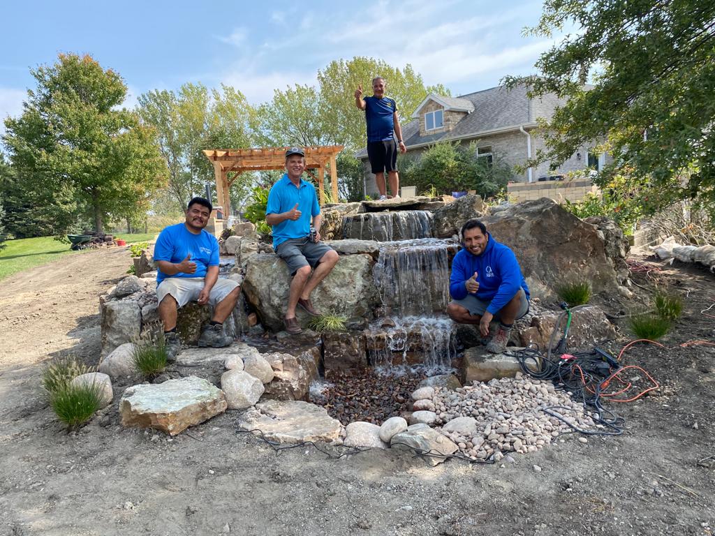 The American Blue Grass Landscaping crew beside a stone waterfall they built
