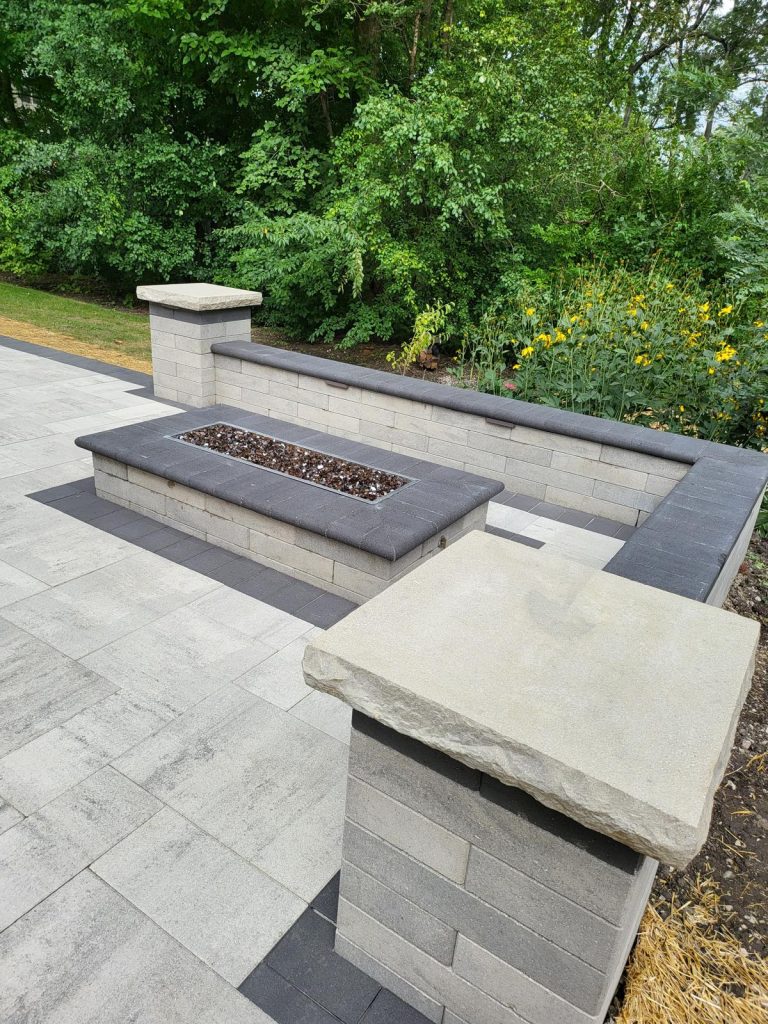Modern fire table and bluestone-capped seat walls on a large-format paver patio