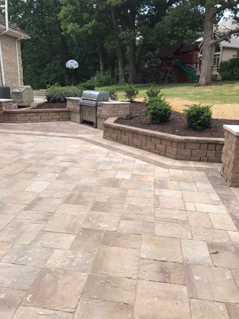 Tumbled paver patio framed by block retaining walls, grill station and new plantings